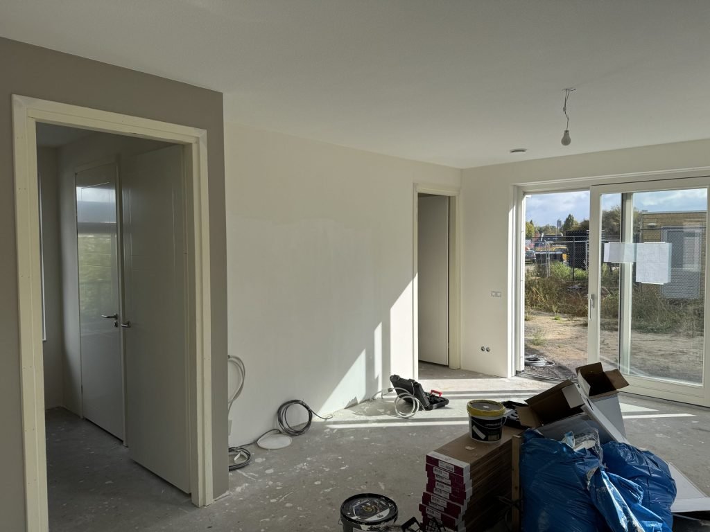 Woonkamer tijdens de afwerking, met verfemmers en materiaal op de betonvloer