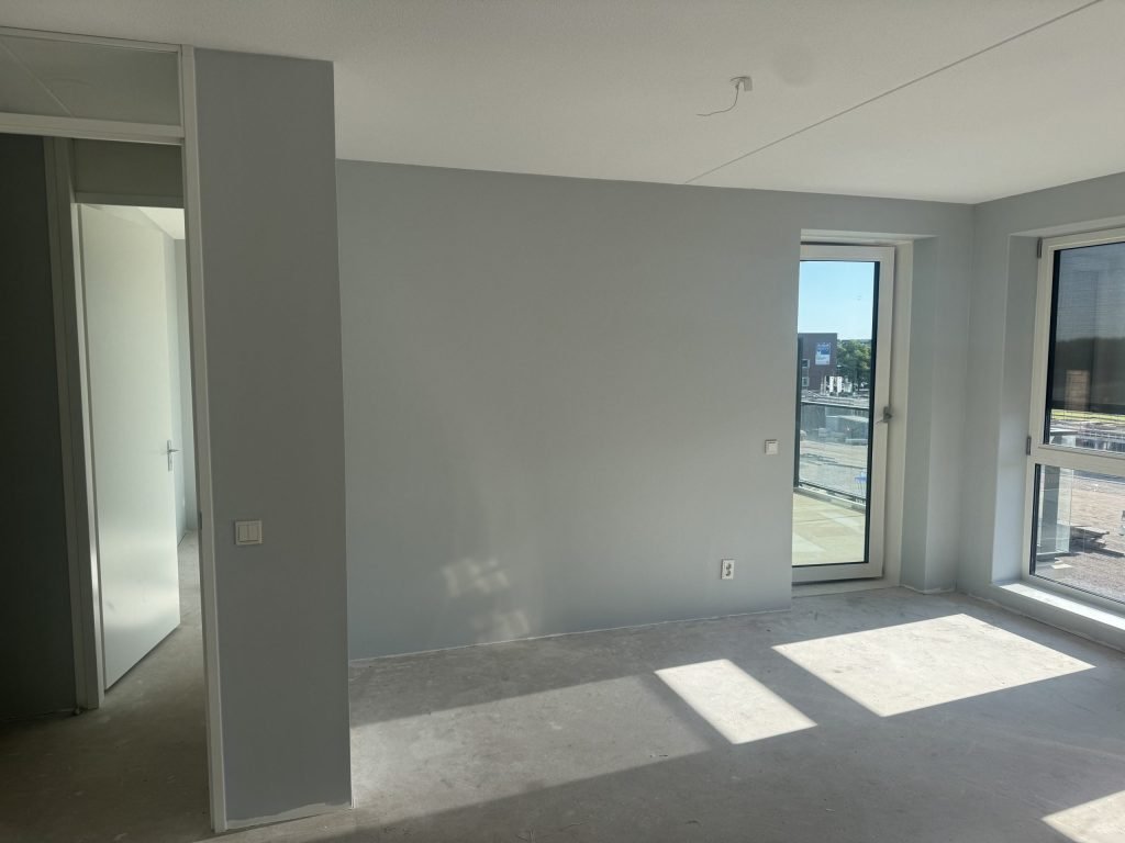 Lege kamer met kale lichte wanden en een balkondeur, klaar voor de behanger