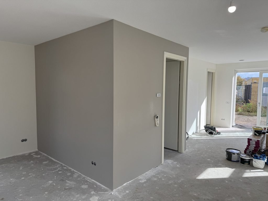 Open woonruimte met een pas gesausde grijze wand en verfemmers bij de tuindeuren