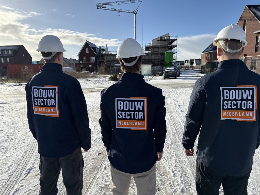 Drie vakmensen van Bouwsector Nederland met witte helm voor een wijk met huizen in aanbouw